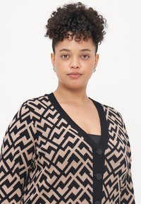 Geometric patterned cardigan in beige and black. Features a deep V-neck, ribbed cuffs, and five black buttons along the front.