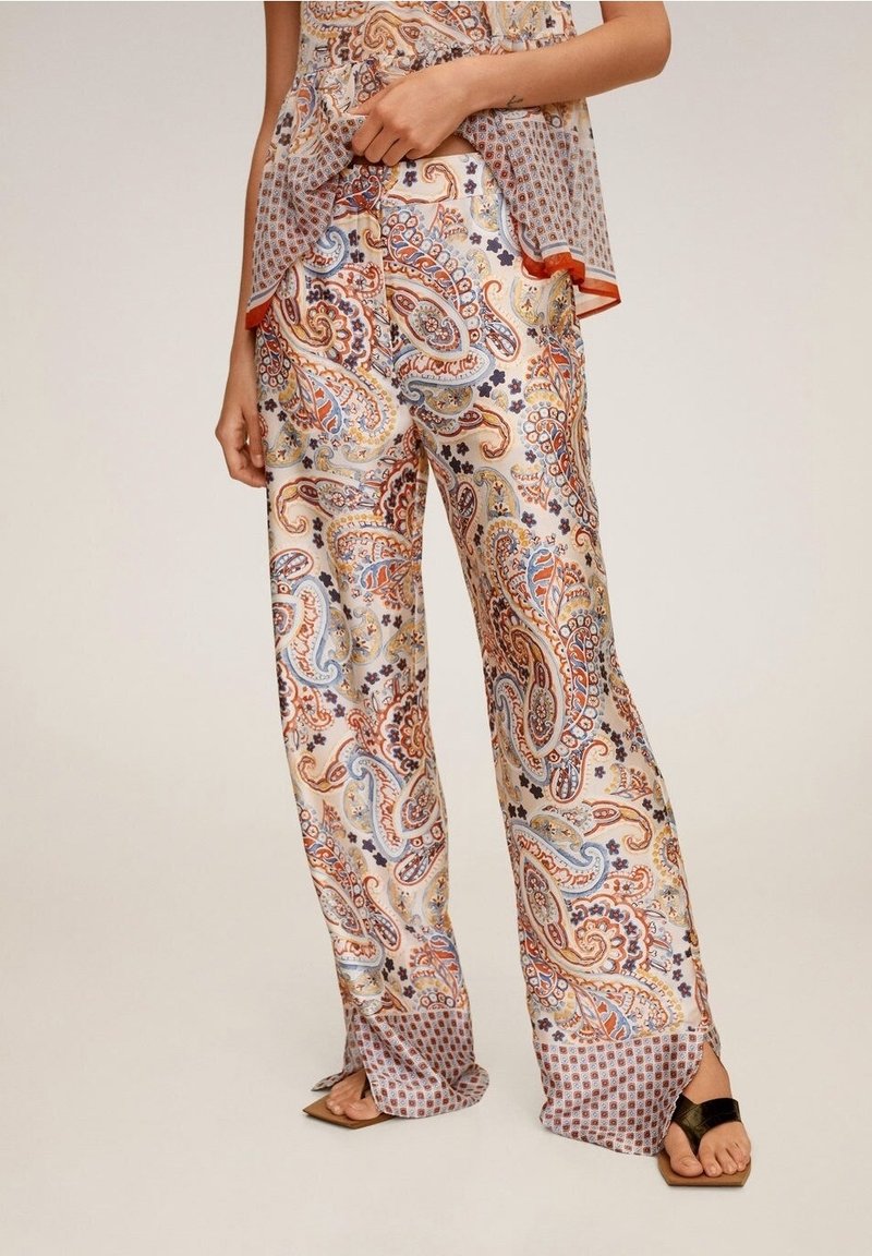 Femme portant un pantalon large et taille haute avec des motifs cachemire colorés et floraux, associé à des sandales à bout ouvert.