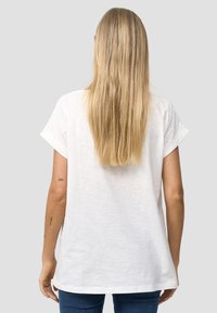 Witte T-shirt met korte mouwen van lichtgewicht stof, met een losse pasvorm en opgerolde mouwen. Huiskleurige armen zichtbaar, met minimale details.