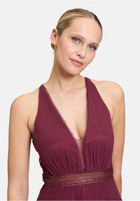 Robe bustier bordeaux avec un décolleté en V profond, un corsage plissé et une ceinture brodée élaborée. Tissu lisse avec une finition élégante.