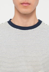 Κάτω μέρος του προσώπου και λαιμός ατόμου που φοράει λευκό και ναυτικό μπλε t-shirt με λεπτές οριζόντιες ρίγες.