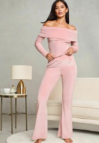 Svetle růžový sametový loungewear set, který zahrnuje top s odhalenými rameny a zvonové kalhoty, s jemným výšivkovým detailem na kalhotách.