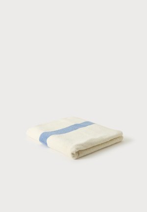 Serviette blanche pliée avec une large bande bleue unique au centre sur un fond clair uni.