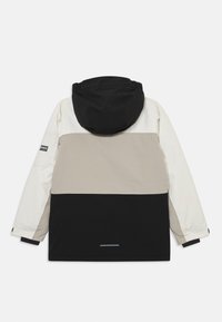 Värviliselt blokeeritud jakk mustas, beežis ja valges; omab kapuutsi, lukuga esiosa ja nähtavat brändi sildi varrukal. Veekindel materjal.