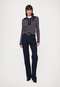 Camiseta de manga larga a rayas azul marino y blanca con cuello con solapa y botones, combinada con vaqueros azul oscuro de pierna recta y zapatos negros.