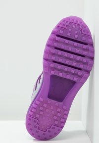 Semelle de chaussure de sport avec une semelle extérieure en caoutchouc violet, présentant des motifs carrés et de profondes rainures horizontales pour une meilleure traction.