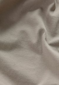 Svetlo béžová bavlnená tkanina s jemnou, hladkou textúrou a miernym elastickým zložením, ktorá vykazuje jemné, rovnomerné tkanie a mierne zvrásnenie.