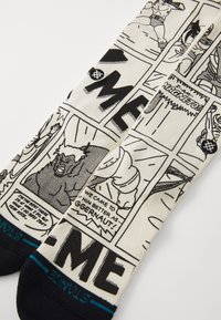 Black and white comic-style socks with text, featuring a cream background. Pattern includes panels with characters and dialogue. Black toe section.