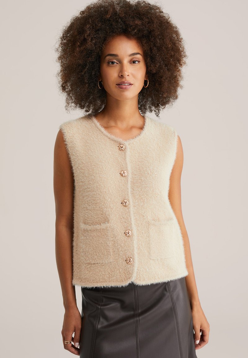 Gilet senza maniche color crema realizzato in morbido materiale lanuginoso, con scollatura rotonda, tasche frontali e chiusure decorative con bottoni.