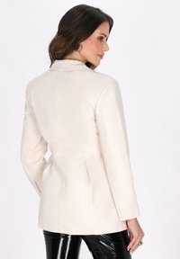 Cremfarbene Imitationsleder-Blazer mit taillierter Passform, strukturiertem Schulterdesign und langen Ärmeln. Der Rücken verfügt über eine Naht mit gerafften Details.