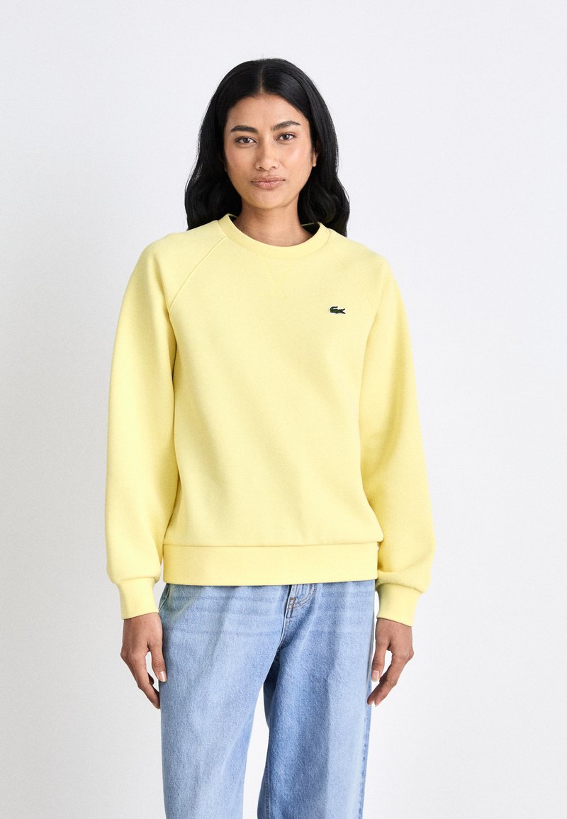 Sweatshirt amarelo feito de tecido macio, com decote redondo, punhos e barra canelados. Pequeno logótipo escuro no lado esquerdo do peito. Corte casual.