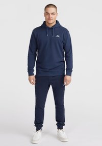 Sweat à capuche bleu marine et jogging assorti en tissu doux. Présente un logo sur la poitrine et les poignets, avec une capuche à cordon réglable.