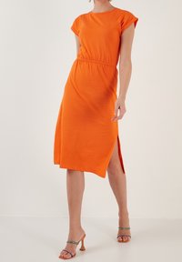 Oranžové šaty s krátkým rukávem a volným střihem, elastickým pasem a bočním rozparkem. Vyrobeno z měkké tkaniny s hladkým povrchem.