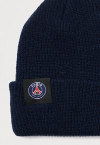 Gorro de malha azul-marinho com aba dobrável, apresentando um patch circular de logo com detalhes vermelhos e azuis que diz "PARIS SAINT-GERMAIN."