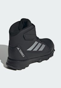 Black hiking boot with synthetic upper, mesh accents, Velcro strap, three gray stripes, and textured rubber sole. Branding on the heel.