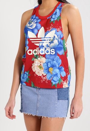 Vrouw draagt een rood Adidas tanktop met grote blauw-witte bloemenprint en een lichtblauwe denim minirok met opgestikte zak.