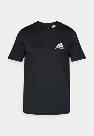 Sort bomulds t-shirt med korte ærmer, prydet med et hvidt adidas-logo og pink tekst på venstre brystområde. Glat tekstur, enkel design.