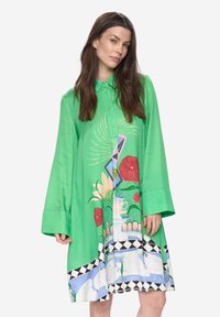 Vestido verde abotonado con mangas largas, con estampados florales y gráficos en varios colores. Textura suave con un diseño fluido.