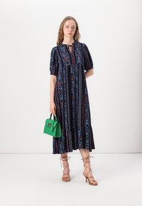 Navy floral dress with short puff sleeves, tiered ruffle hem, and cinched neckline. Green handbag with structured design and top handle.