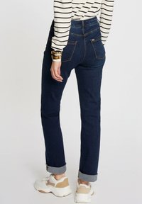 Vaqueros de mezclilla azul oscuro con un diseño ajustado, puños enrollados y dos bolsillos traseros, combinados con unas zapatillas blancas con acentos beige.