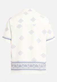 Chemise à manches courtes en tissu blanc avec un motif géométrique de losanges bleus et une bordure florale au niveau de l'ourlet. Présente un col standard et un empiècement dans le dos.
