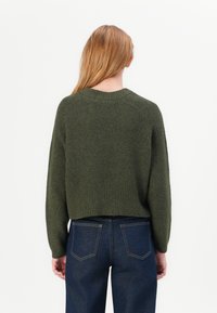 Maglione verde lavorato a maglia con orlo a coste, scollatura tonda e spalle scese, abbinato a jeans di denim scuri. Vista posteriore mostrata.
