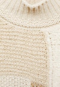 Strickpullover in Creme mit hohem Rippkragen. Enthält verschiedene Texturen und Muster, darunter glatte und erhabene Stickdesigns.