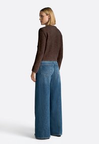 Maglione marrone con texture e maniche lunghe abbinato a jeans in denim blu a vita alta e gamba larga, dotati di tasche posteriori e una vestibilità comoda.