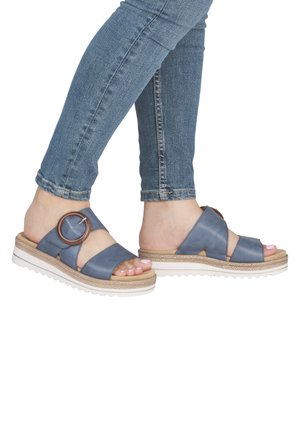 Blue leather slide sandals with a circular accent, woven midsole, and white textured outsole. Designed with crisscross straps.