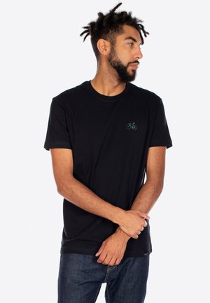 Schwarzes Baumwoll-T-Shirt mit einem kleinen grünen Fahrrad-Graphic auf der linken Brust. Kurzärmel und runder Ausschnitt. Getragen mit blauen Jeans.