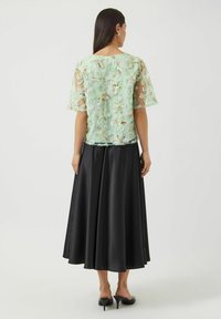 Lysegrønn bluse med blomsterbroderi, gjennomsiktig materiale og korte ermer, kombinert med et svart satengskjørt. Glatt tekstur og flytende design.