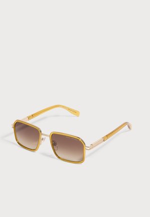 Verres rectangulaires marron dégradé avec fines montures jaunes et branches jaunes assorties de lunettes de soleil de créateur posées sur une surface blanche.