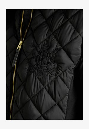 Schwarze gesteppte Jacke mit goldfarbenem Reißverschluss und besticktem Logo mit Kronendetail. Glatte Textur mit gepolsterten Bereichen und kontrastierenden Strickseiten.