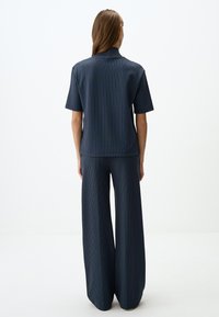 Granatowy, dwuczęściowy zestaw w prążki, składający się z koszulki z krótkim rękawem i szerokich spodni. Materiał ma gładką teksturę.