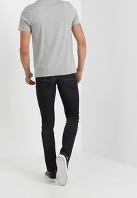 Camiseta gris de manga corta, jeans negros ajustados y zapatillas negras con suelas blancas. Acentos de cuero y costuras en contraste en los jeans.