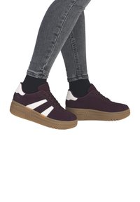Purple sneakers with white accents, featuring a textured upper, round toe, and a thick gum sole, paired with grey jeans.