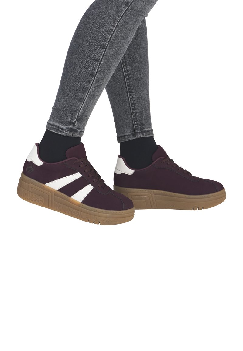 Purple sneakers with white accents, featuring a textured upper, round toe, and a thick gum sole, paired with grey jeans.