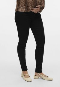 Jeans skinny negros con una textura suave, combinados con tacones slingback de cuero patent crema que presentan una punta cuadrada y un tacón bajo.