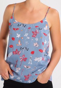 Ärmlös blå blus med blommönster som har olika röda och vita bladmönster. Tillverkad av ett mjukt tyg med spagettiband.