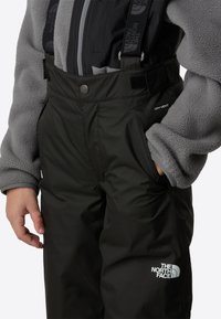 Fekete vízálló nadrág állítható vállpántokkal és előzsebbel. "DRYVENT" felirattal és fehér logóval a lábon.