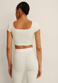 Bílý ribbovaný crop top s krátkými rukávy ve tvaru rukávku a čtveratým zadním dílem, doplněný o odpovídající ribbované legíny. Hladká textura s přiléhavým střihem.