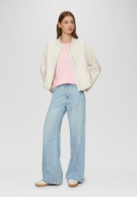 Helle beigetone Bomberjacke, rosa Oberteil und weit geschnittene hellblaue Jeans. Das Outfit zeichnet sich durch glatte Texturen und eine lockere Passform aus.