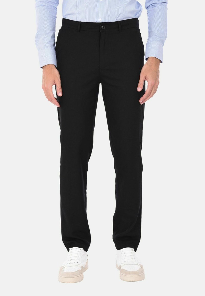 Pantaloni neri con una vestibilità sartoriale, dotati di chiusura con bottone e tasche laterali. Indossati con sneaker bianche per un contrasto.