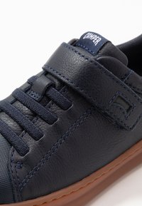 Jūras zilas ādas sporta kurpes ar auduma auklām, Velcro siksnu, zilām šuvēm un brūnu gumijas zoli; teksturēti akcenti uz pirkstu zonas.