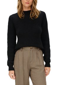 Schwarzer gerippter Strickpullover mit rundem Hals und langen Ärmeln, kombiniert mit tanfarbenen Hahnentritt-Hosen mit Falten und einem Knopf.