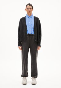 Zwarte cardigan over een blauw gestreept shirt, grijze sweatpants en witte sneakers. Relaxte pasvorm; knoopdetails op het shirt en de cardigan.