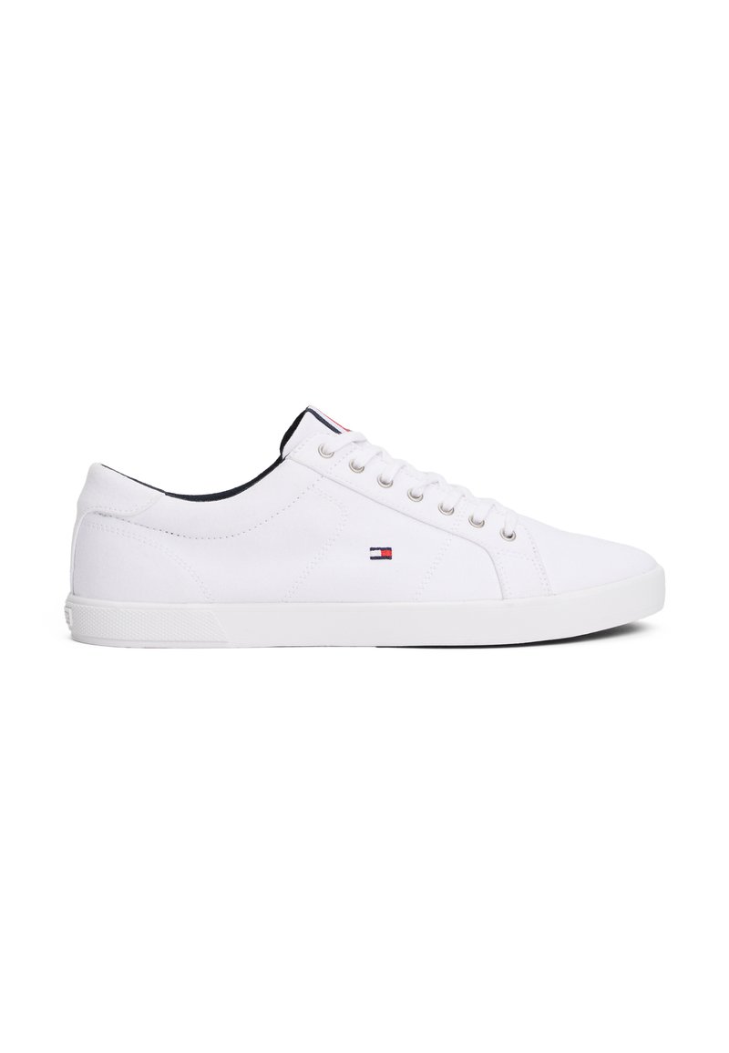 Zapatillas de lona blancas con un diseño de caña baja, cordones en la parte delantera y suela de goma. Presentan un pequeño logo en el lateral y acentos negros en contraste.