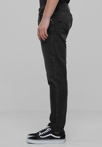 Mustat farkut, jotka ovat slim fit -mallia, klassisella viiden taskun designilla ja metalliosilla. Yhdistetty mustiin urheilujalkineisiin.
