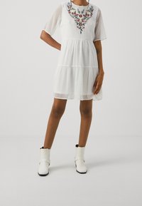 Vestido blanco con mangas cortas, lunares texturizados y bordado floral en el escote. Combinado con botas blancas hasta el tobillo.
