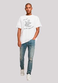 White cotton t-shirt with a graphic print of a dog on a surfboard. Paired with light blue distressed jeans and white sneakers.